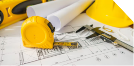 A close-up of construction tools, including a yellow tape measure, caliper, hard hat, blueprints, and a level, placed on an architectural floor plan.